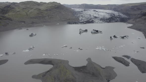 Aerial view overlooking blackened ice blocks on the Solheimajokull glacier lagoon - tracking, drone