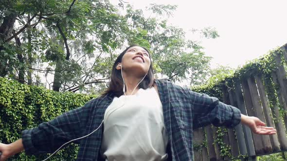 Young Asian woman deeply in a forest to enjoy and listen to music on smartphone.