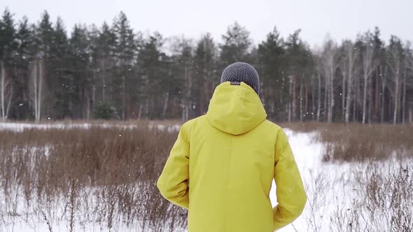A man in a yellow jacket runs across a field covered with snow