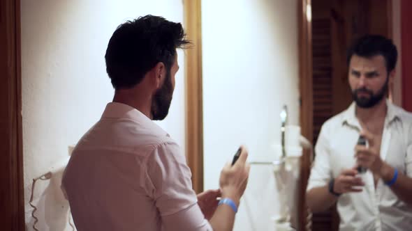 Man Hairstyling On Mirror. Man Using Hair Spray In Hotel Room For Pompadour. Hairstyle With Hand.