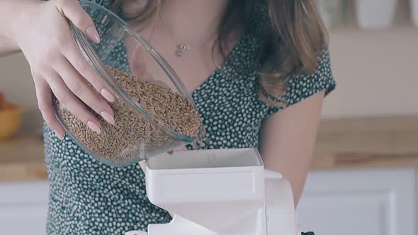 Woman Fills Home Flour Grinder with Raw Wheat in Kitchen