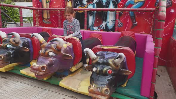 Red hair child girl riding mechanical bull at amusement park. Slow motion