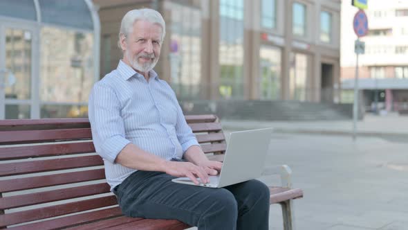 Old Man with Laptop Showing Thumbs Up Sign While Sitting Outdoor on Bench