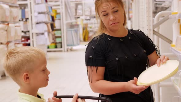 A Woman and a Little Boy Together Choose Plastic Dishes in a Large Hypermarket