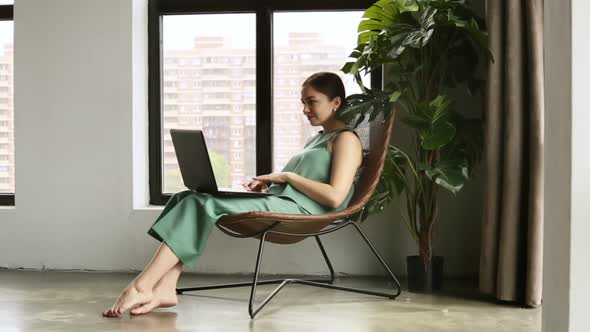 Beautiful Young Woman is Using Laptop While Sitting in Apartment Room During Quarantine Iroi