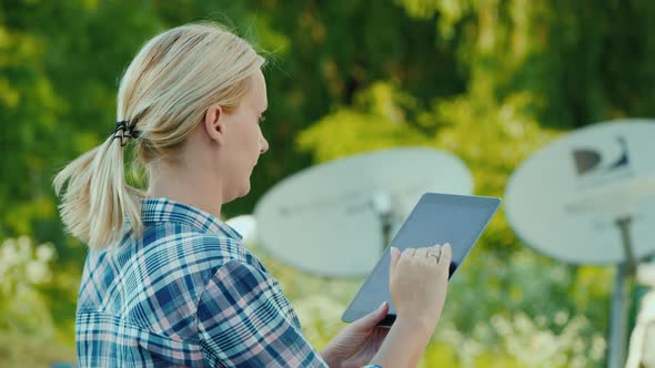 Side View of Woman Sets Up a Satellite Dish, Uses a Tablet