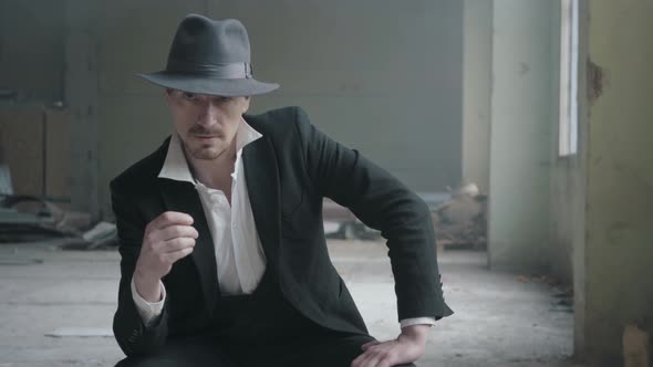 Portrait Handsome Confident Man in a Hat Turning the Coin in the Fingers Sitting in an Abandoned