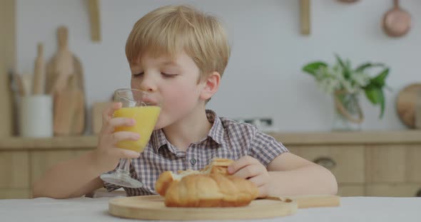 Preschool Boy Eating Bun and Drinking Orange Juice at Wooden Kitchen, Hungry Kid Chewing Homemade