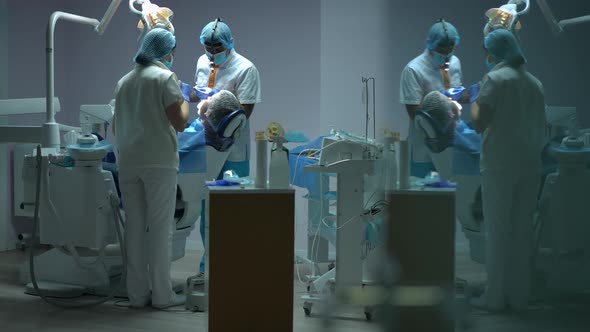 Wide Shot Concentrated Professional Doctor and Assistant Treating Man in Dental Chair Reflecting in