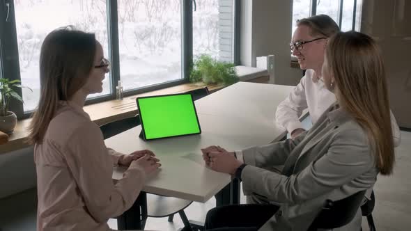 Three aspiring entrepreneurs are discussing a project with a green mockup screen on a tablet