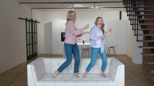Happy Family Senior Mom Having Fun with Adult Daughter Dancing on Sofa in Living Room