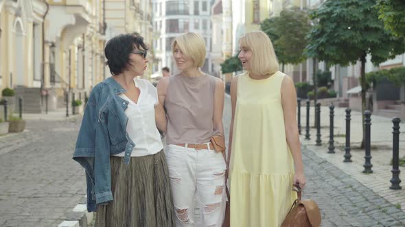 Three Caucasian Mid-adult Women Standing on City Street on Summer Day and Talking. Portrait of