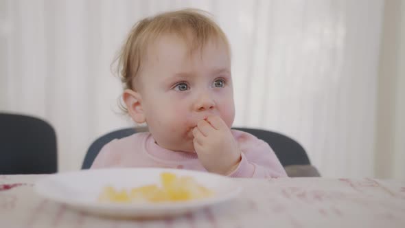 Cute baby eating an orange next to a table