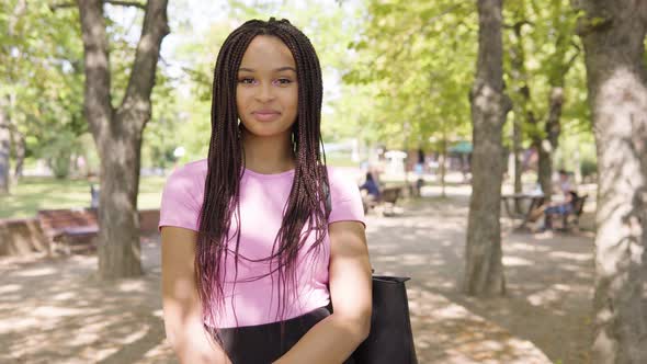 A Young Black Woman Smiles at the Camera in a Crowded Park on a Sunny Day