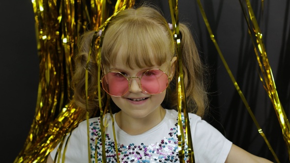 Happy Child Jumping, Playing, Fooling Around in Shiny Foil Fringe Golden Curtain. Little Blonde Girl