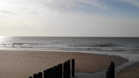 Tranquil Beach With Rolling Waves And Old Wooden Pilings On Shore In Brouwersdam, Netherlands - aeri