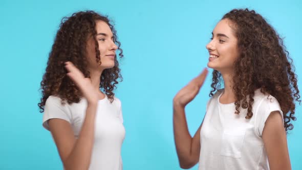 Two Smiled Beautiful Curly Caucasian Female Twins in White Tshirts Giving High Five to Each Other