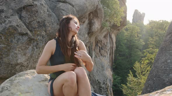 An Attractive Young Woman in a Blue Silk Dress is Seated on Rocky Terrain Relaxing Outdoors