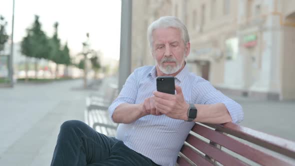 Old Man Using Smartphone While Sitting Outdoor