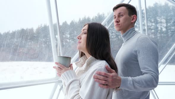 Man Pets Woman on Shoulder Enjoying Drink at Home in Winter