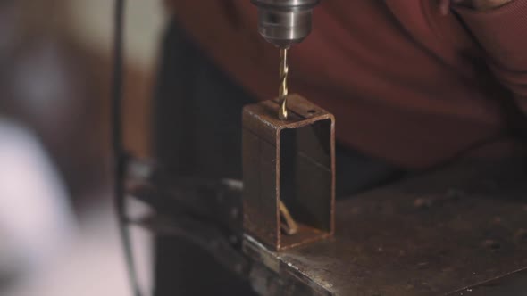 Man Hard Worker Drills Metal with an Electric Drill in Garage