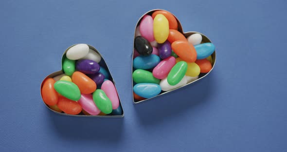 Video of overhead view of multi coloured sweets in two heart shapes over blue background