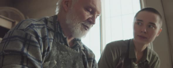 Elderly Man Teaching Young Student How to Use Pottery Wheel