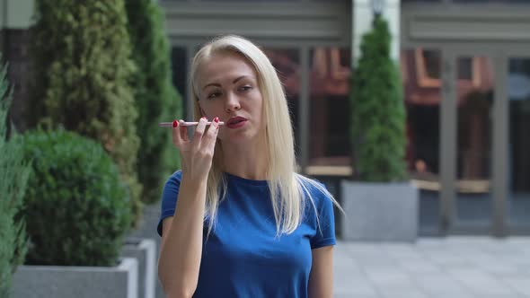 Portrait of a Charming Young Woman Talking on Her Smartphone on Speakerphone. Blonde in a Blue