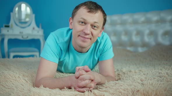 Smiling man lying on bed in bedroom and looking at camera