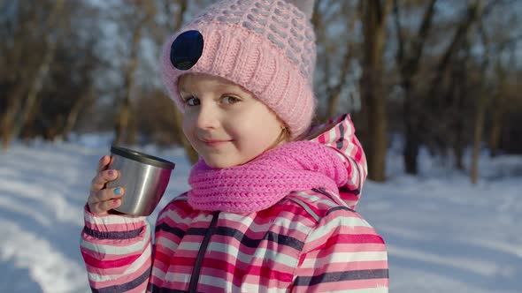 Child Girl Kid Drinking Hot Drink Tea From Cup on Snowy Road in Winter Park Christmas Holidays