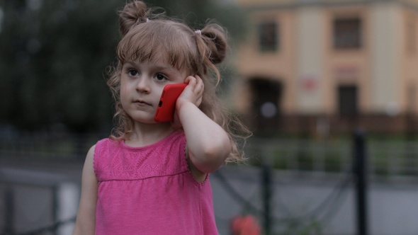 Child Girl Talking By Smartphone Outdoors. Kid in Pink Dress Talking By Mobile Phone on City Street