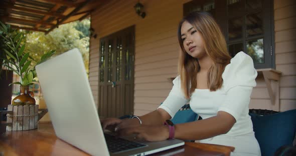 Asian girl in white dress sitting on terrace enjoying view and using laptop in midday