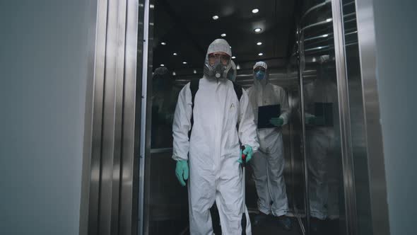 Covid-19 Spreading. People in Protective Biological Suit Exiting Elevator in Business Center