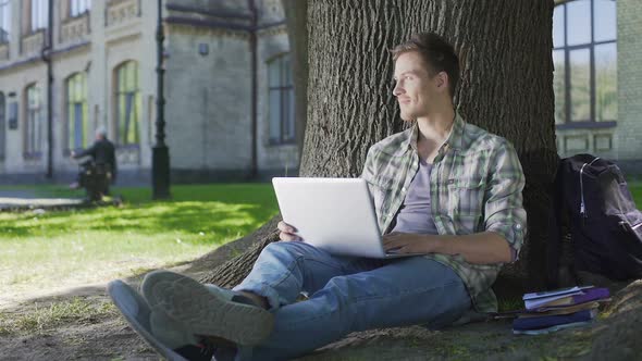 Senior Student Working on His Project on Laptop Sitting Under Wide Tree, Campus