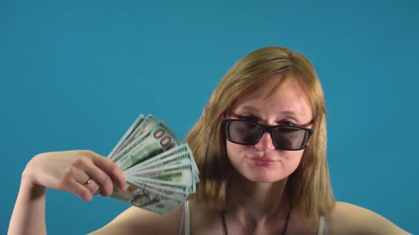 Girl in Glasses Waving Dollars on a Blue Background