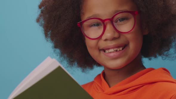 African American school girl in eye glasses reads book and smiles at camera