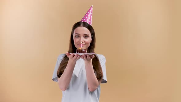Happy Young Cheerful Birthday Girl with a Present Wearing Party Head on a Beige Background