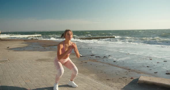 Athletic Woman Squats with Jump on Seafront Washed By Waves