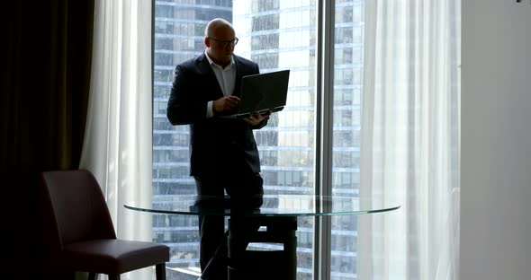 Male Lawyer Is Working in His Office, Standing Near Window and Holding Open Laptop in Hands