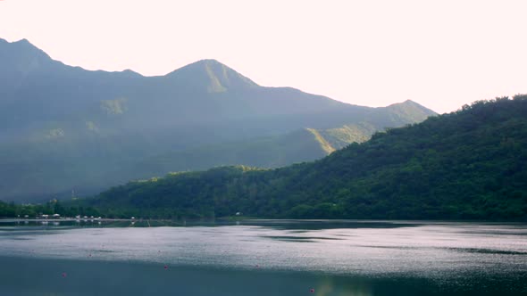 Rays of sunlight breaking over mountains and lighting up a cool and calm lake in early morning