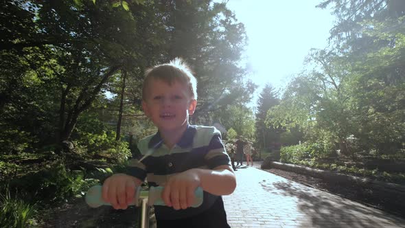 Little Boy Rides Scooter in the Park on Sunny Day