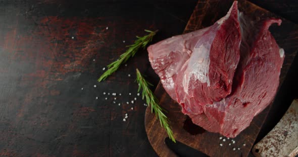 A Piece of Raw Beef with Rosemary on the Table. 