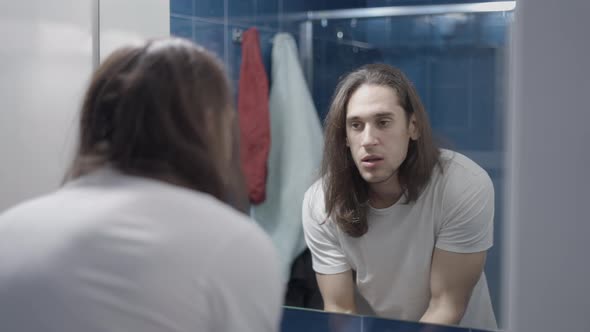 Longhaired Man Looking at His Teeth Right After Brushing Them in Front of a Bathroom Mirror Slow