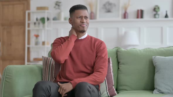 African Man having Neck Pain while Sitting on Sofa