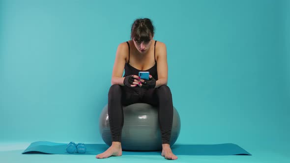 Athlete Taking Break to Use Smartphone and Relax on Toning Ball