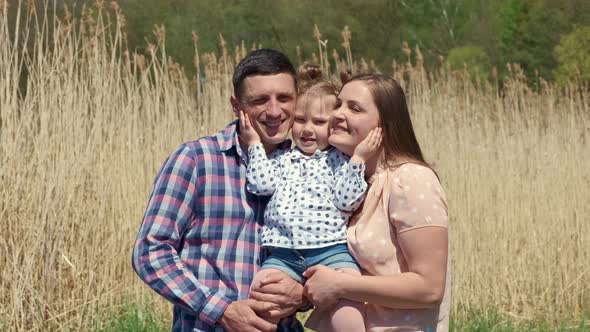 Happy Young Couple with a Little Girl in Their Arms on Nature on the Background of Reeds