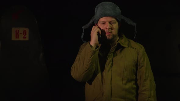 Russian Man in a Hat with Earflaps, Talking on the Phone in a Dark Basement and Decides Matters