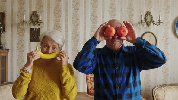 Mature Caucasian Married Couple Holding Banana and Oranges Simulating Smile and Eyes