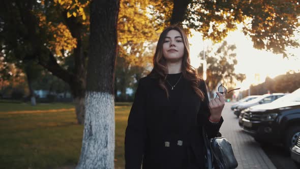 A Stylish Young Girl with Long Luxurious Hair Goes Along a City Street with a Bag on Her Hand and