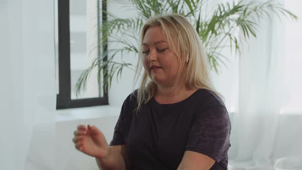 Blonde Confident Overweight Woman Puts Wireless Headphones in Her Ears and Drinks Water From the